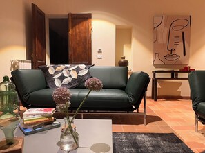 Ein Wohnzimmer mit einem grünen Ledersofa, einem Couchtisch mit Büchern und einer Vase, einem Gemälde an der Wand und einem Fliesenboden.