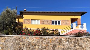Un bâtiment jaune agrémenté d’éléments en pierre, un mur de pierre au premier plan et un ciel bleu clair.