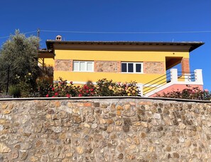 Ein gelbes Gebäude mit Steindetails, eine Steinmauer im Vordergrund und ein strahlend blauer Himmel.