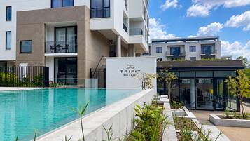 Un bâtiment moderne doté d’une piscine, d’une enseigne indiquant « TRIFIT WELLNESS », et d’une entrée en verre.