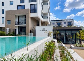 A modern building with a swimming pool, a sign reading 'TRIFIT WELLNESS,' and a glass entrance. - The Rosebank Suite One Rosebank Private Terrace (Johannesburg)
