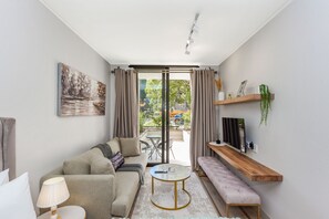 Un salon moderne comprenant un canapé, une table basse, un banc, un téléviseur posé sur une étagère en bois et une porte-fenêtre coulissante donnant sur un espace extérieur.