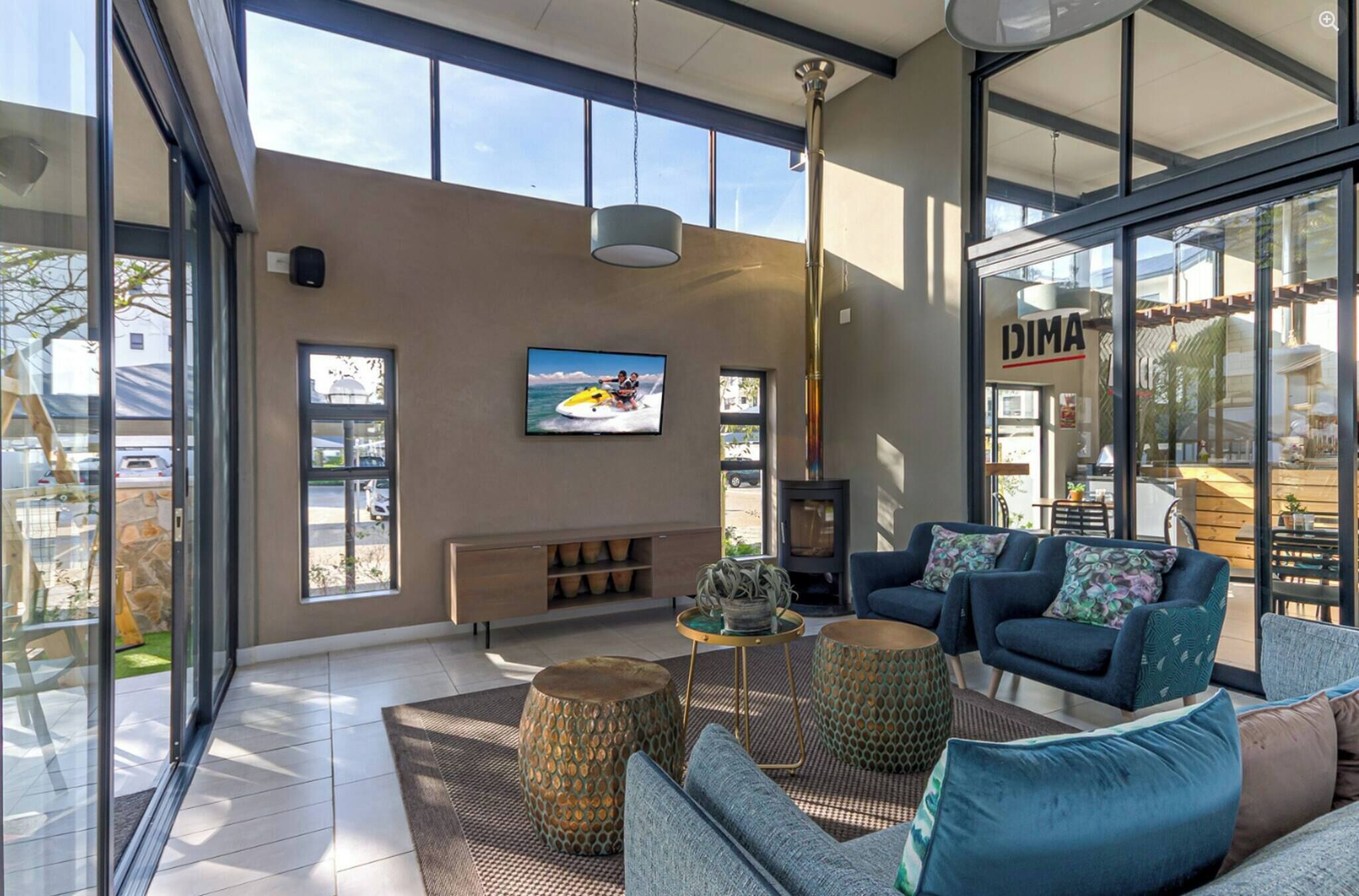 A modern living room with a large TV, comfortable seating, a fireplace, and large windows.