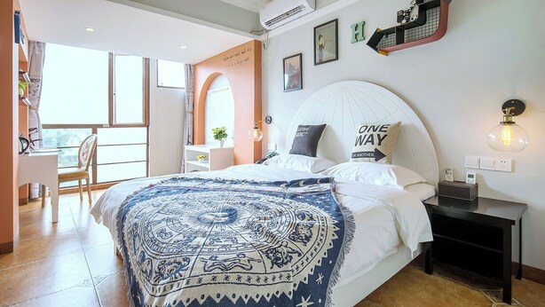 A bedroom with a large bed, a bedside table with a lamp, a chair, a desk, and a window. - Summer Inn Sanya (Sanya)