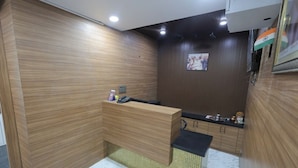 Un espace d’accueil avec un comptoir de réception en bois, un téléviseur fixé au mur et une petite étagère contenant divers objets.