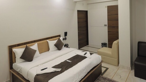 Une chambre moderne avec un grand lit, un ventilateur de plafond, un éclairage encastré, une porte en bois et un petit coin salon.