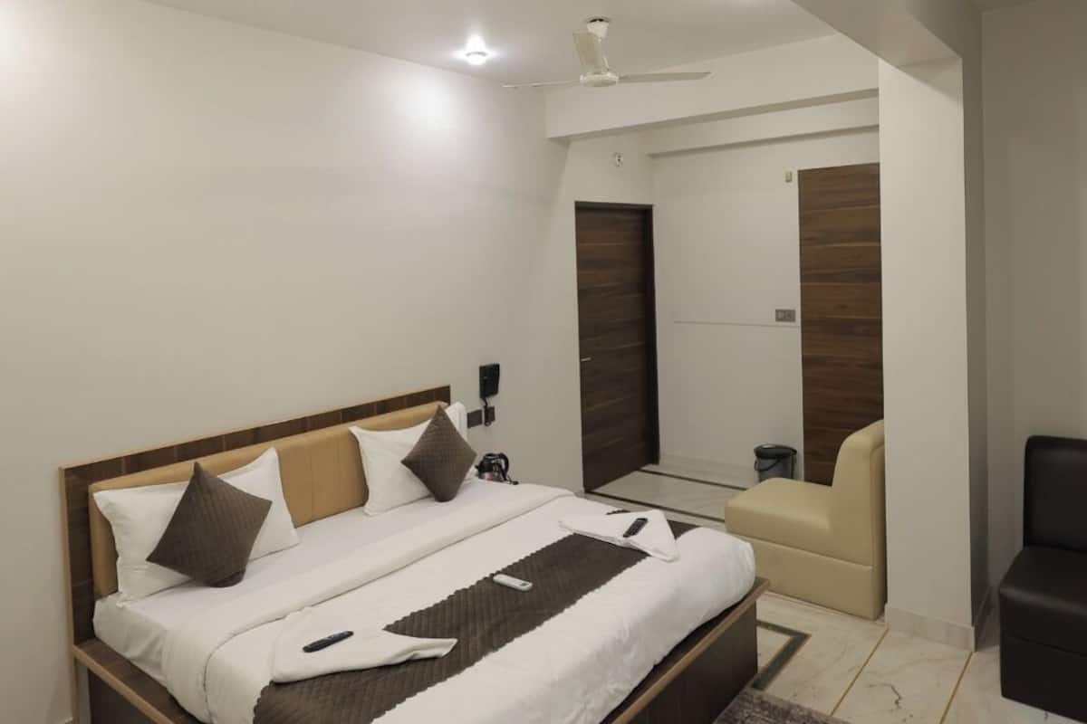 A modern bedroom with a large bed, a ceiling fan, recessed lighting, a wooden door, and a small seating area.