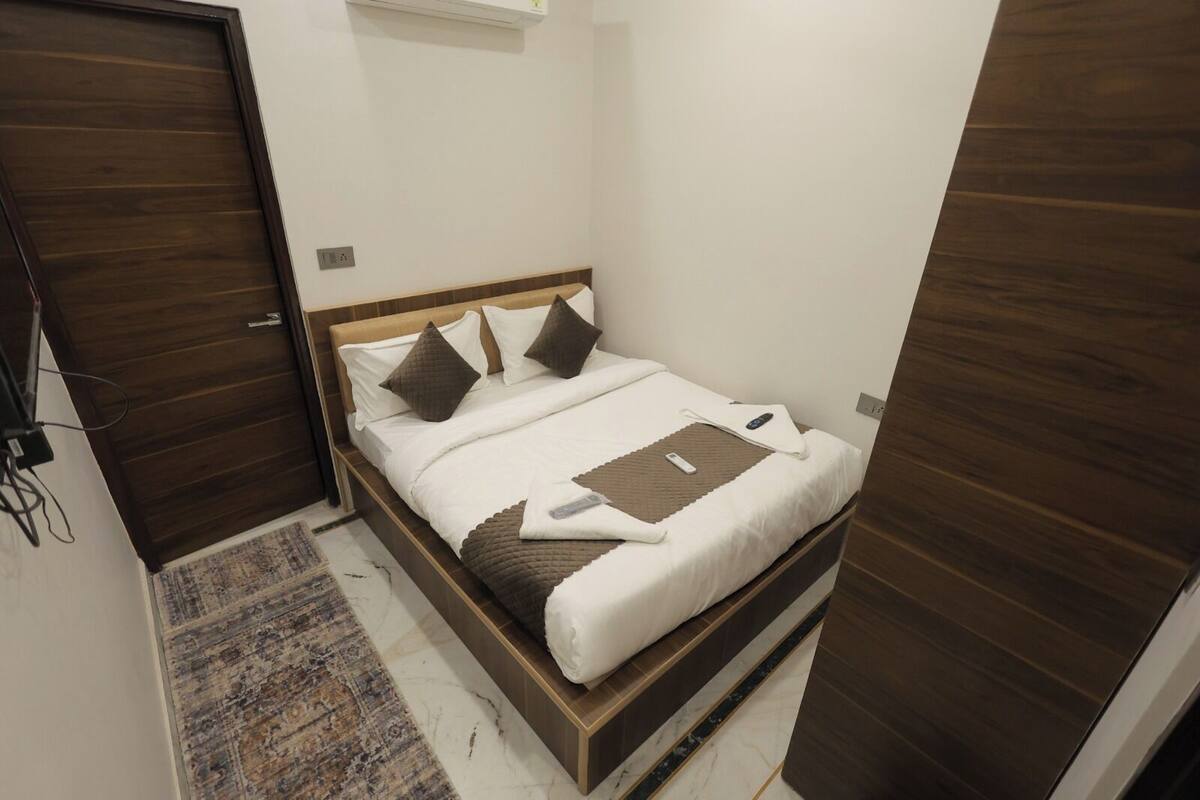 A bedroom with a bed, pillows, a blanket, and a remote control.