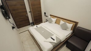 Une chambre d’hôtel avec un lit, une table de chevet, une armoire et une télécommande posée sur le lit.