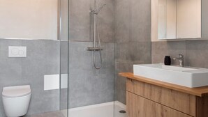 A modern bathroom with a glass-enclosed shower, a white sink, and a wooden vanity.
