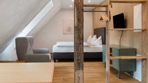 A modern loft bedroom with a sloped ceiling, a bed, a desk, and a chair.