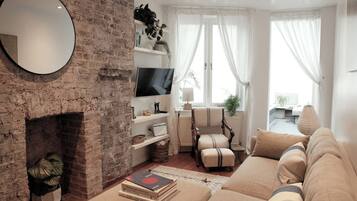 A living room with a brick wall, a flat-screen TV, a sofa, a chair, and a fireplace.