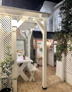 Ein überdachter Patio-Bereich mit Esstisch, einer Bank und Kübelpflanzen.