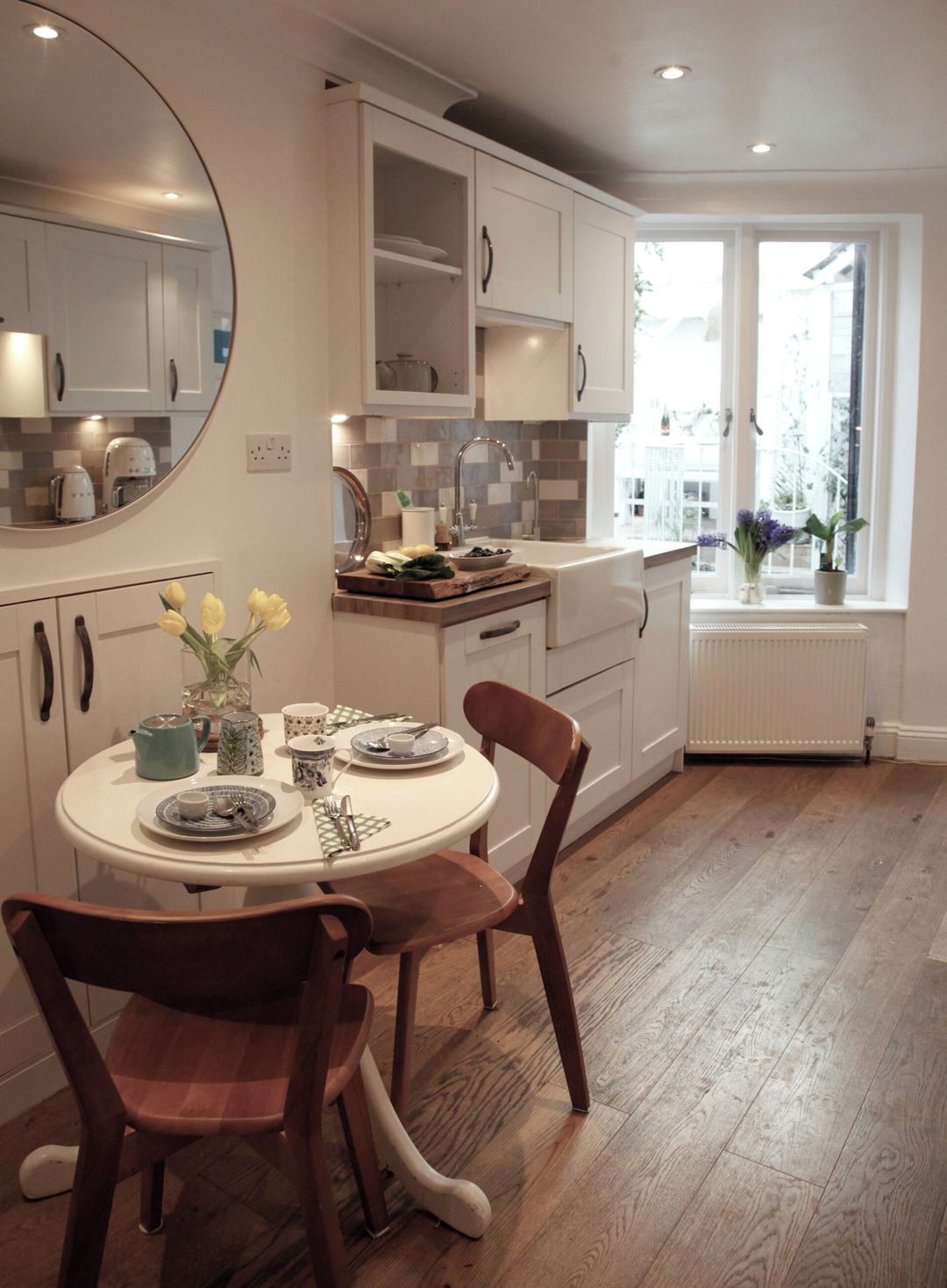 A modern kitchen with white cabinetry, a round dining table, and a view of the outdoors through a window.