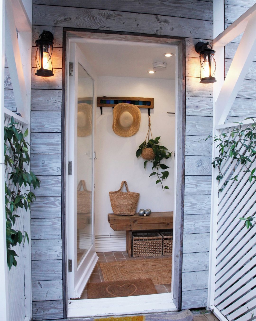 A wooden exterior with a glass door entrance, a hanging basket, a woven basket, and a wall-mounted hat rack.