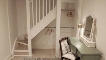 A room with a staircase, a vanity with a mirror, and a chair.