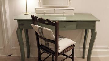 A room with a green desk, a chair with a cushion, a lamp, and a mirror.