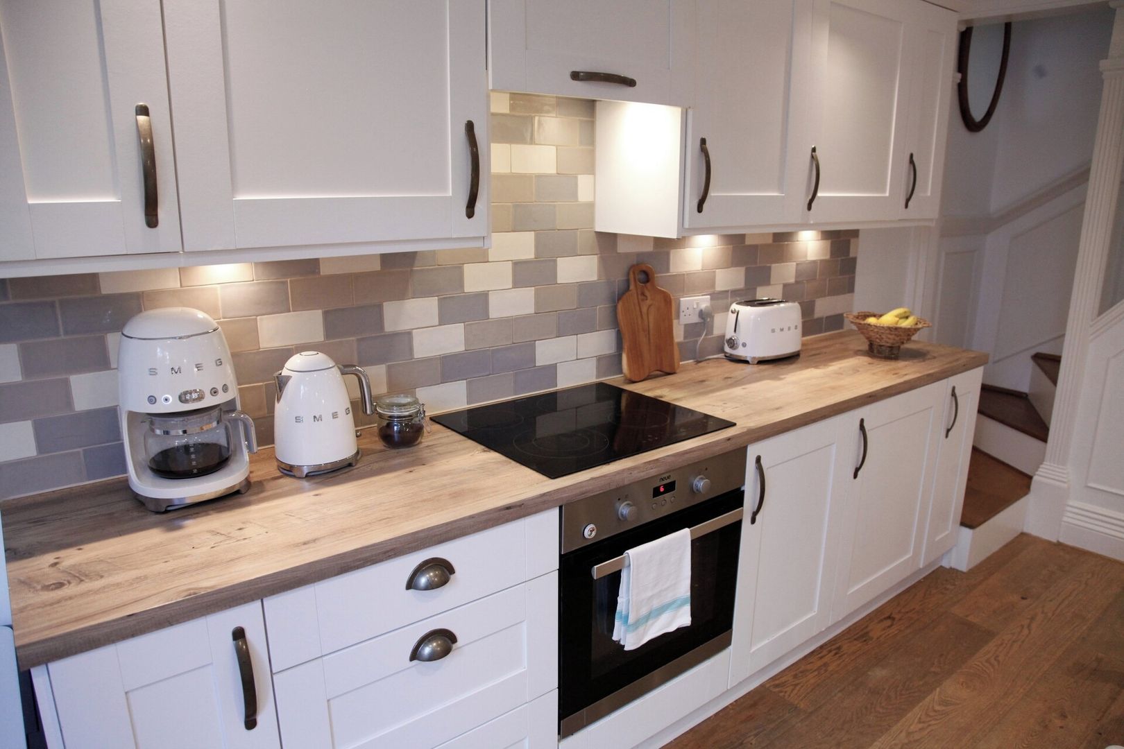 A modern kitchen with white cabinets, a black stovetop, a coffee maker, and a toaster.