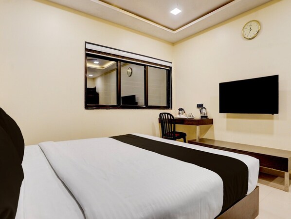 Habitación de hotel con una cama, un escritorio con silla, un televisor y un reloj en la pared.