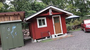 Uma pequena cabana vermelha com porta de madeira, janela e um pequeno alpendre.