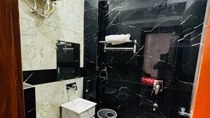 A compact bathroom with a toilet, sink, and shower area, featuring black marble walls and white fixtures. - Hotel The Amaresh (Panipat)