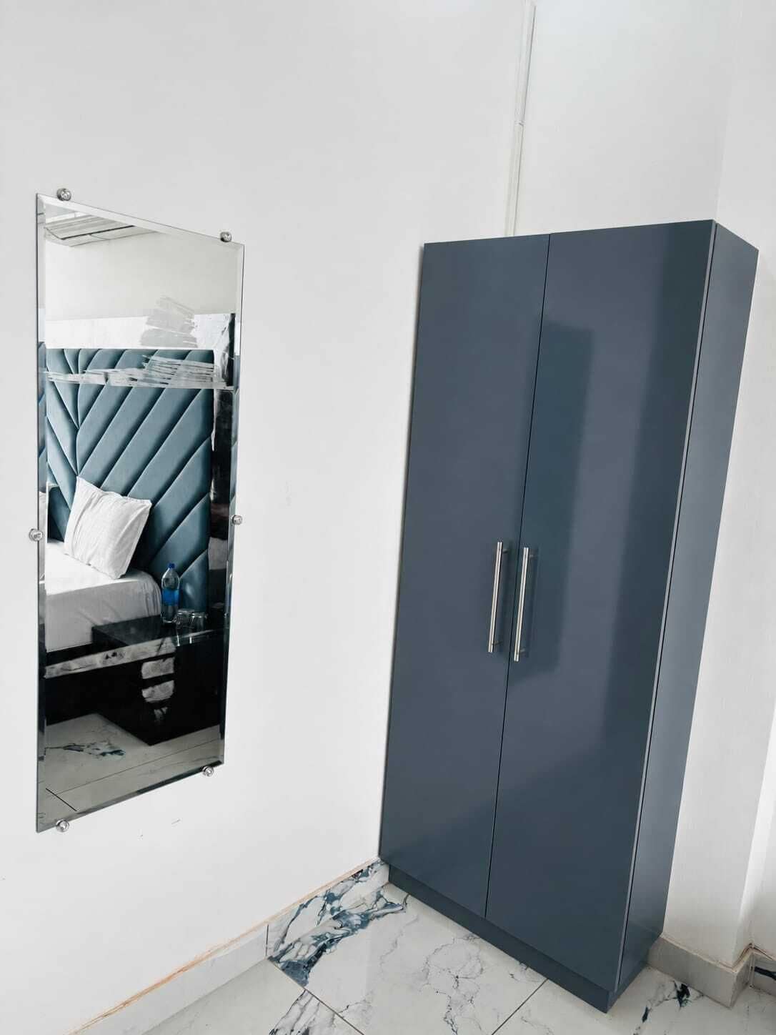 A room with a bed, a wardrobe, and a mirror reflecting the bed.