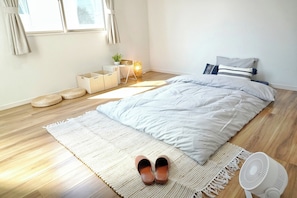 Un dormitorio con cama, una mesita de noche con lámpara, un ventilador y una ventana con cortinas.