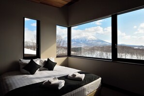 Ein Schlafzimmer mit Bett, Kissen und Handtüchern, große Fenster mit Blick auf die Berge.