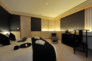 Ein modernes Hotelzimmer mit einem großen Bett, einem Schreibtisch, einem Stuhl und einer Massageliege.