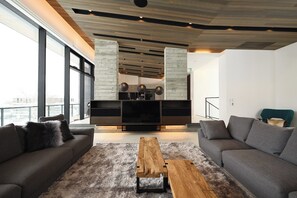 Ein modernes Wohnzimmer mit großem Fernseher, grauen Sofas, einem Holztisch und Blick auf die Stadt.
