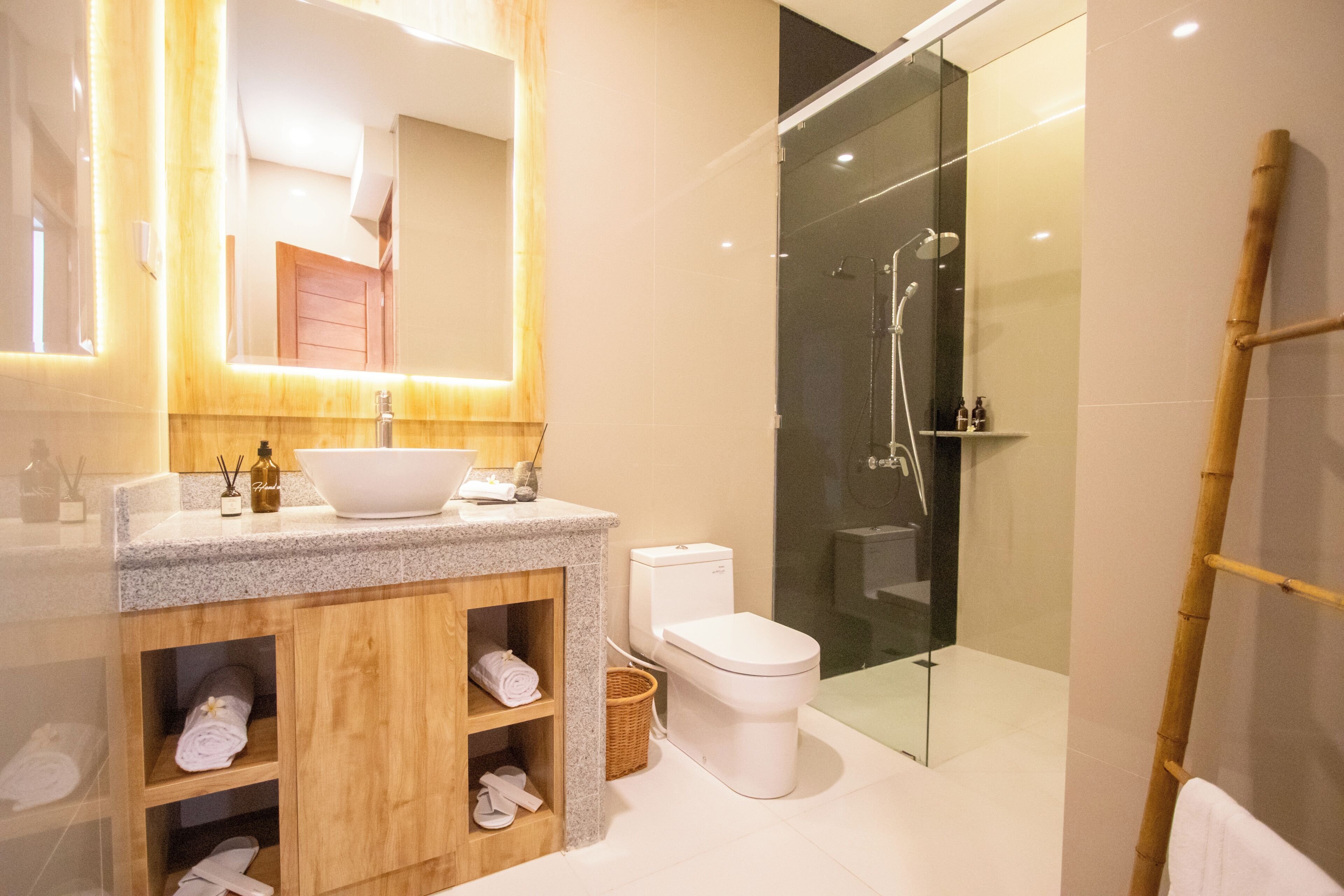 Un baño moderno con encimera de granito, mueble de tocador de madera, inodoro blanco y cabina de ducha con mampara de vidrio.