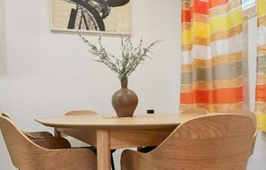 Ein Essbereich mit einem runden Tisch, vier Holzsesseln, einer Pflanzvase und einem gestreiften Vorhang.