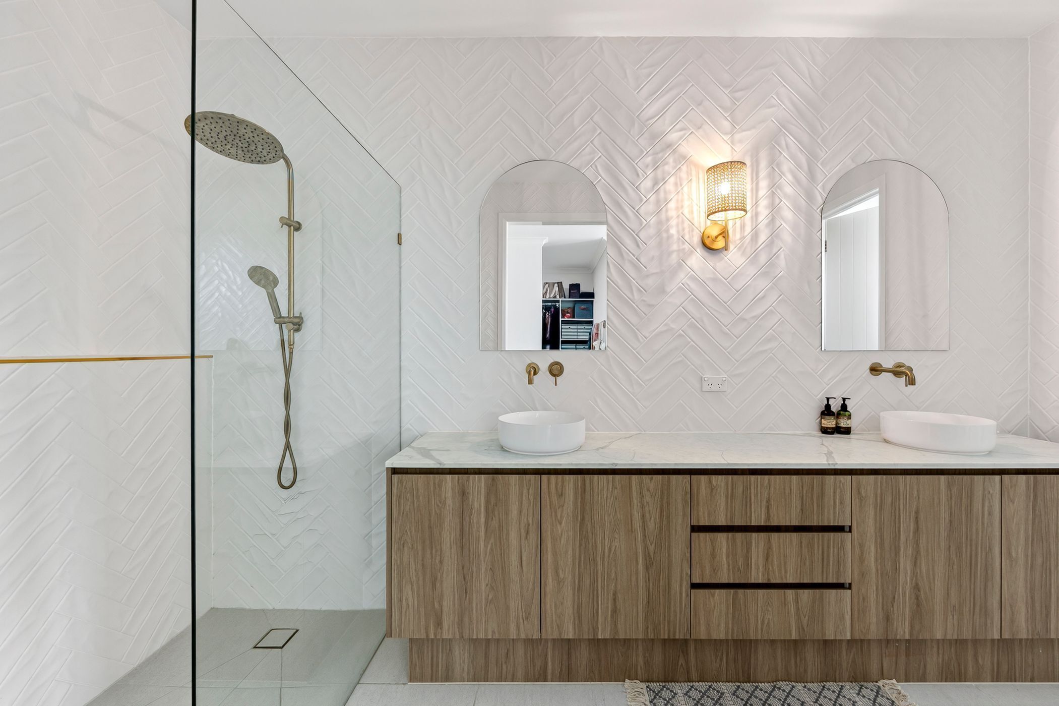 Ein modernes Badezimmer mit einer Duschkabine aus Glas, einem Holzbadezimmer-Möbelkorpus mit zwei Waschbecken und einer Wand mit Zickzackmuster.