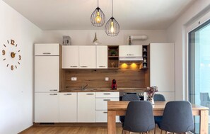 Eine moderne Küche mit weißen Schränken, einer Holzauskładung, einem Esstisch mit Stühlen, Pendelleuchten und einem großen Fenster.