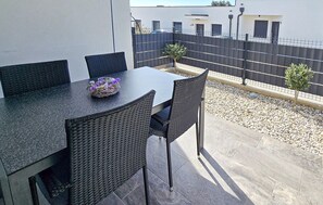 Eine Terrasse im Freien mit Tisch, Stühlen, einer kleinen Zierpflanze und einem Zaun.