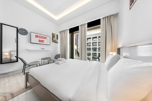 Ein Hotelzimmer mit einem großen Bett, einem Schreibtisch, einem Sessel, einem Fernseher und einem Fenster mit Vorhängen.