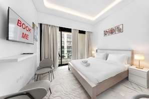 Ein modernes Hotelzimmer mit einem großen Bett, einem Schreibtisch mit Stuhl, einem Fernseher und einem Balkon mit Vorhängen.