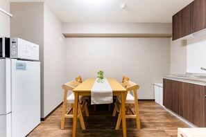A compact kitchen with a dining table, wooden chairs, a refrigerator, and a microwave. - 42 square meters | Deluxe Twin Room accommodates  / Kagoshima City Kagoshima (Kagoshima City)