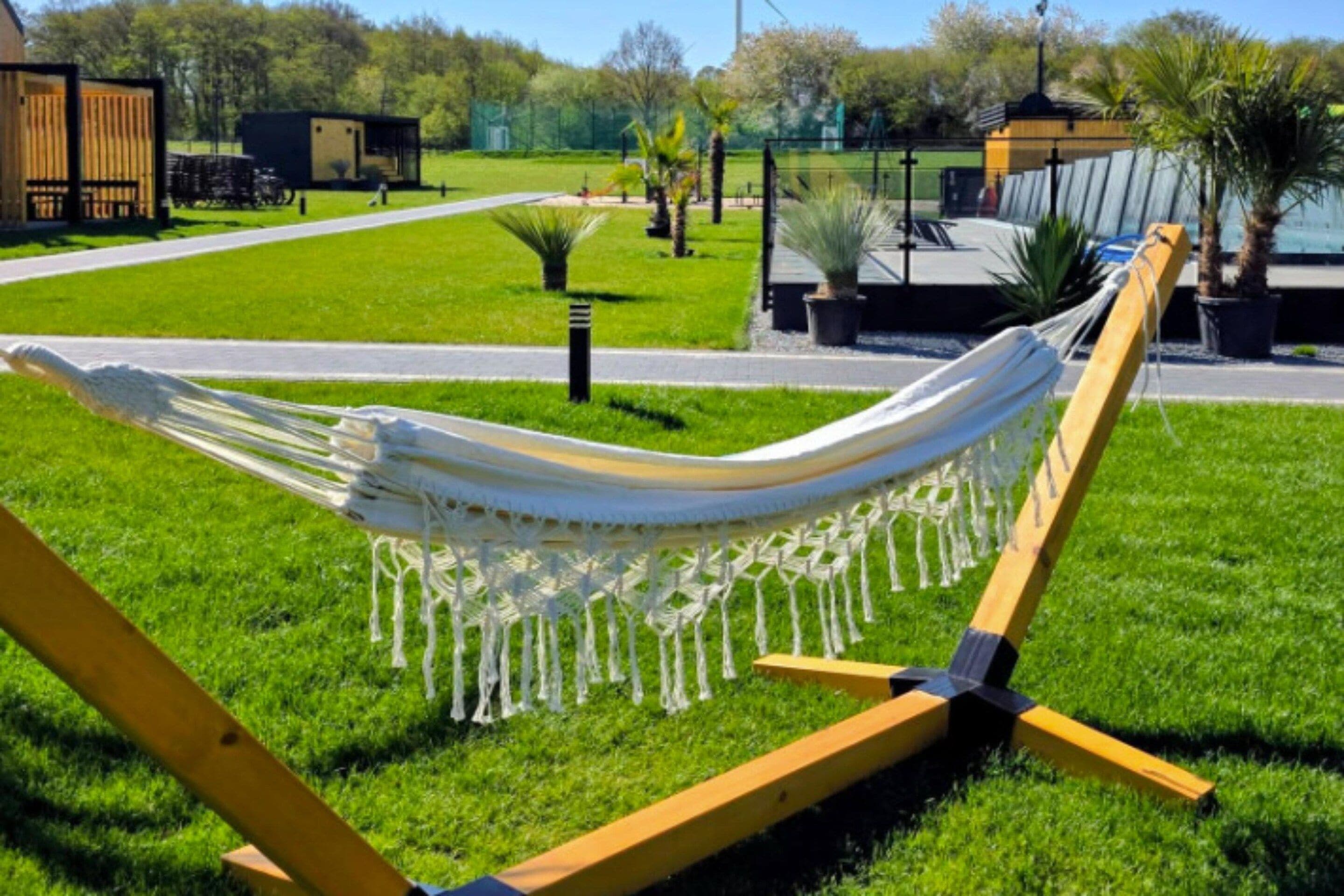 Een hangmat bevestigd tussen twee gele palen in een grasveld, met een heldere lucht.