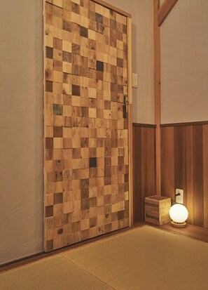 Eine Holztür mit Schachbrettmuster, ein kleiner Holztruhe mit Lampe und Tatami-Boden.