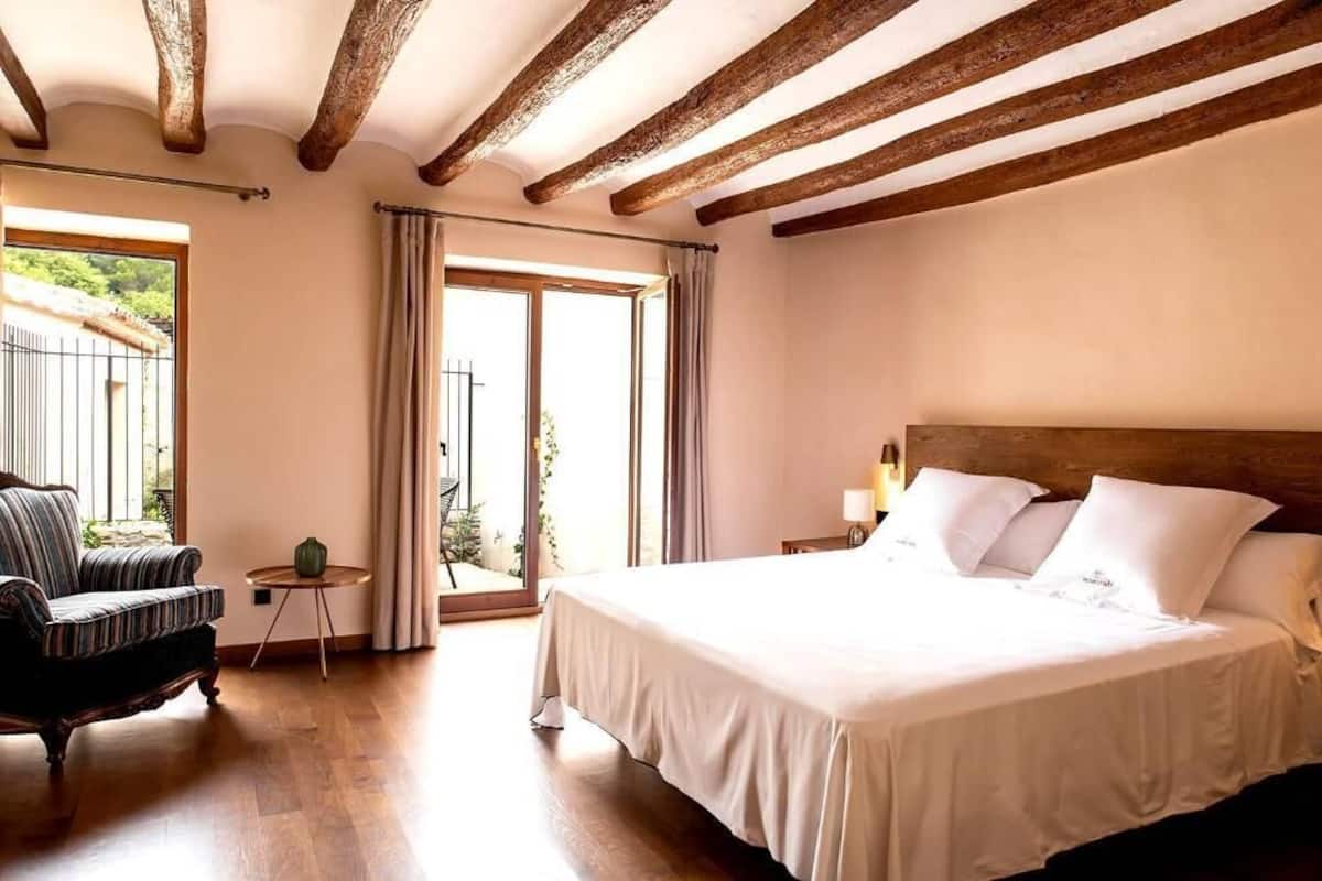 A bedroom with a large bed, a chair, a small table, and a window with curtains.