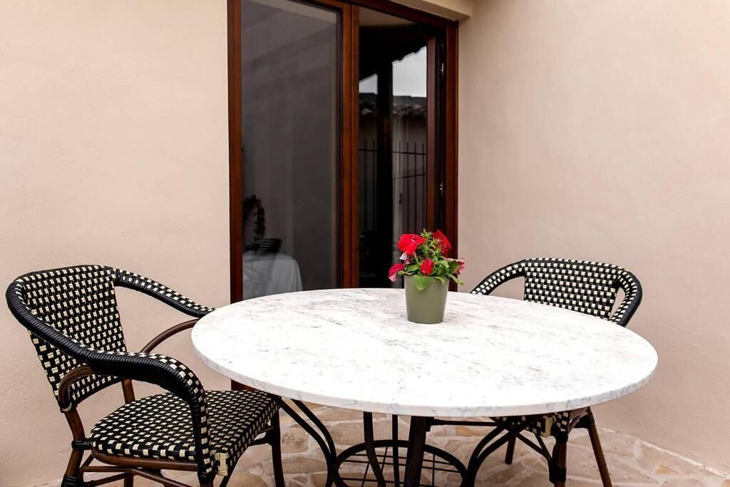 A round table with four black wicker chairs, a potted plant with red flowers, and a glass door leading to an outdoor area.