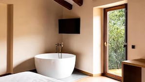 A modern bathroom with a freestanding bathtub, a mounted TV, and a sliding glass door leading to a balcony. - Hotel Montrubí 1771 (Font-Rubi)