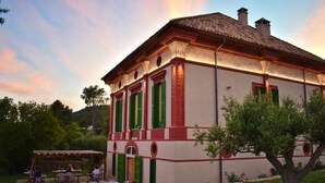 A building with a tiled roof, green shutters, and a patio area with tables and chairs. - Hotel Montrubí 1771 (Font-Rubi)