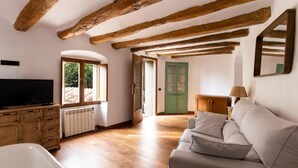 A room with exposed wooden beams, a television, a sofa, a wicker cabinet, and a green door. - Hotel Montrubí 1771 (Font-Rubi)