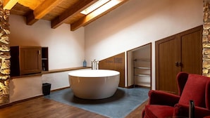 A modern bathroom with a large bathtub, wooden beams, stone wall, and a red chair. - Hotel Montrubí 1771 (Font-Rubi)