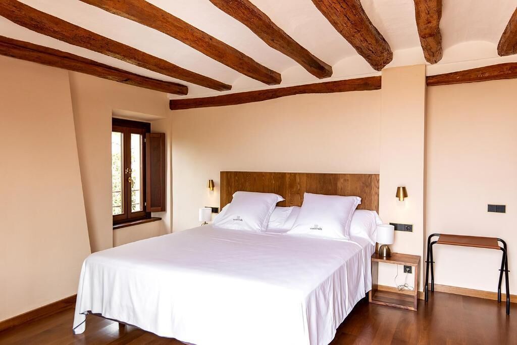 Une chambre avec un plafond en bois, un lit avec une literie blanche, des lampes de chevet et une fenêtre.