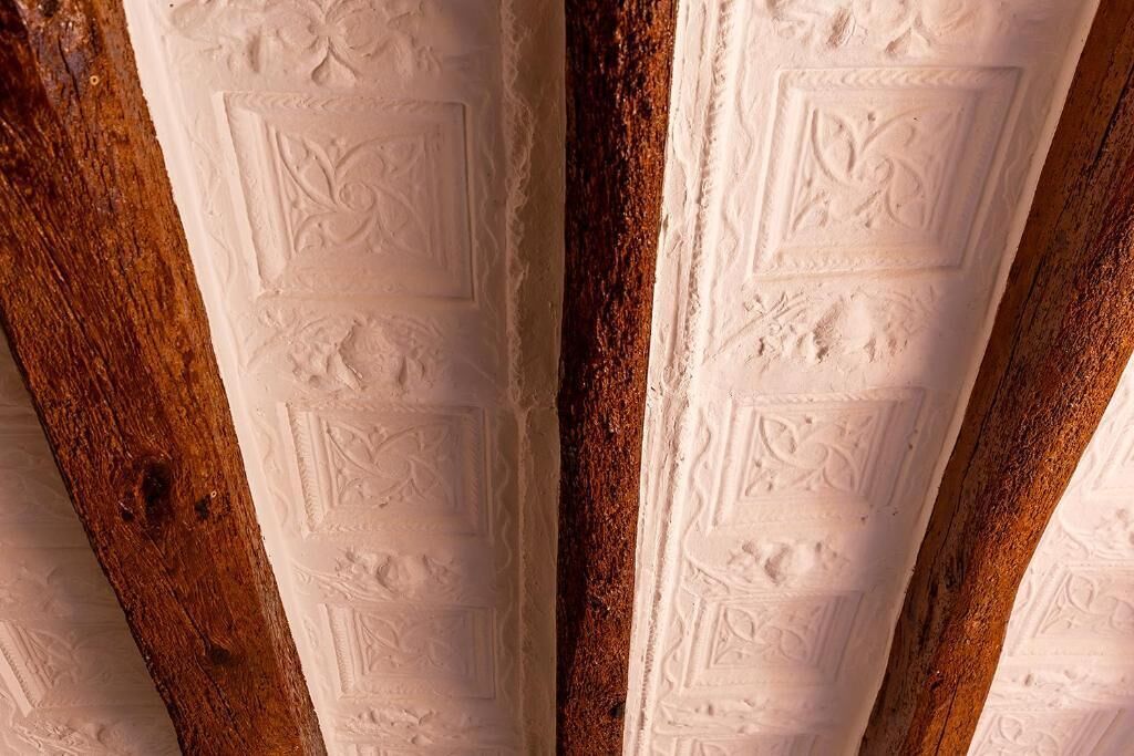 A close-up of a ceiling with intricate embossed patterns and wooden beams.
