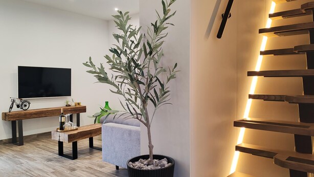A modern living room with a flat-screen TV, a wooden bench, a grey sofa, and a potted plant. - 2 bedroom stunning home in Selca (Selca)