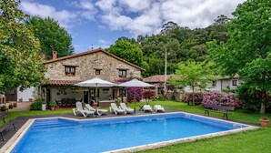 Una casa de piedra con piscina, mobiliario exterior y abundante vegetación.